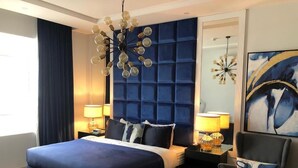 A modern hotel room with a large bed, two bedside tables with lamps, a blue accent wall, and a decorative ceiling light fixture. - Dana Serviced Apartments2 (Riyadh)
