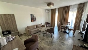 Ein modernes Wohnzimmer mit einer Couch, einem Couchtisch und Sesseln. Es gibt einen Fernseher, eine Holzkommode und ein Bild an der Wand.