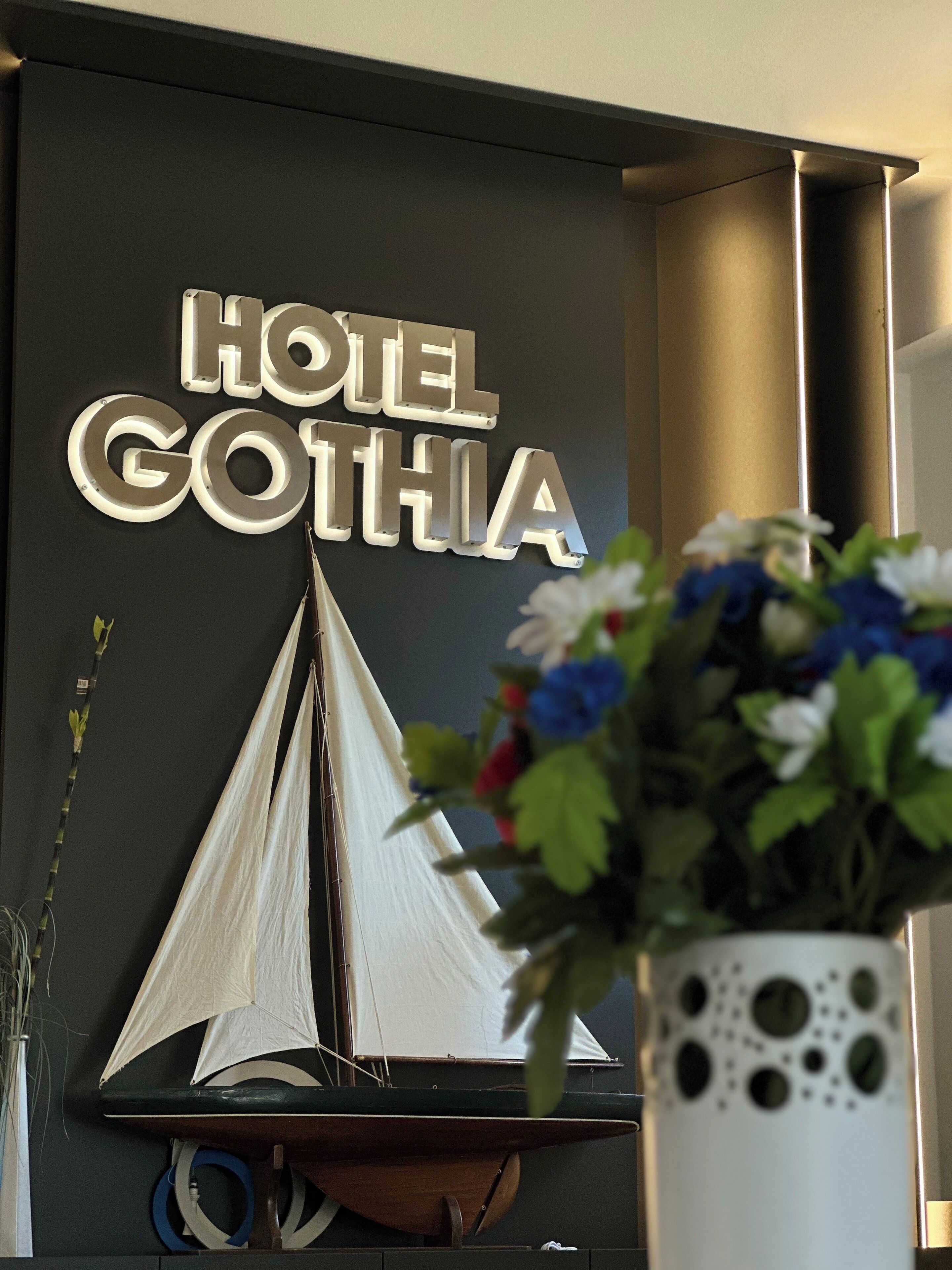 A sign reading "HOTEL GOTHIA" with a sailboat decoration and a potted plant with flowers.