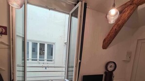 A room with a large window, a wooden ceiling beam, a clock, and a tiled floor. - La Sainte Madeleine (Gap)