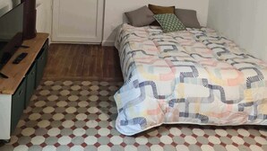 A bedroom with a bed, a desk, a chair, a clock, a door, and a hanging light fixture. - La Sainte Madeleine (Gap)