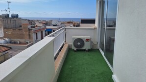 Un balcón con césped artificial, un equipo de aire acondicionado y vistas a la ciudad.