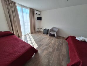 A hotel room with two beds, a chair, a TV, and an air conditioning unit. - Room-triple Double Room (Terrasini)