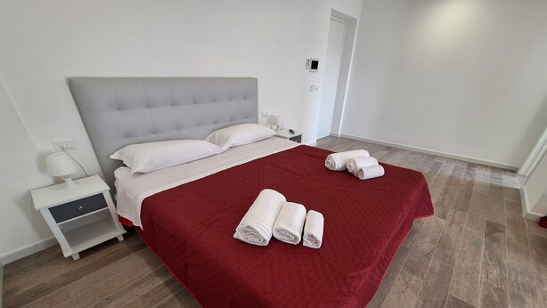 Una cama bien hecha con una colcha roja, almohadas blancas y dos toallas enrolladas sobre la cama.