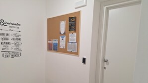 Un pasillo con un tablón de anuncios mostrando varios avisos y un cartel de bienvenida en la pared.