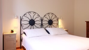 A bed with a white bedspread and two pillows, flanked by two wall-mounted metal flower-like light fixtures. - Bel Respiro, an enchanting getaway in the heart of Monteleone hillside (Roncofreddo)