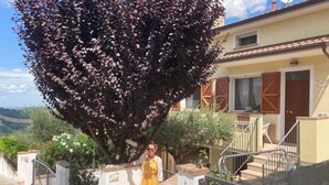 A person standing in front of a building with a staircase and a tree. - Bel Respiro, an enchanting getaway in the heart of Monteleone hillside (Roncofreddo)