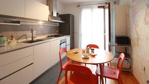 A compact kitchen with white cabinets, a stainless steel range, and a dining area with a wooden table and red chairs. - Bel Respiro, an enchanting getaway in the heart of Monteleone hillside (Roncofreddo)