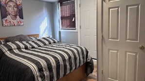 A bedroom with a bed, a window with blinds, a door, and a painting on the wall.