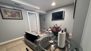 A modern kitchen with a glass dining table, a built-in oven, and a flat-screen TV mounted on the wall.