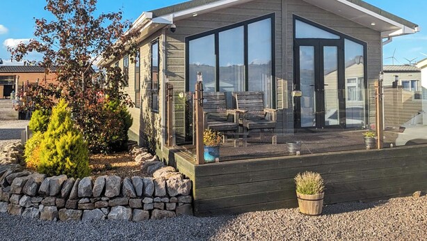 A modern house with a large glass front, a deck with chairs, and a stone wall. - 3 bedroom accommodation in Moota, Near Cockermouth (Moota, Near Cockermouth)