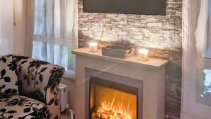 A living room with a fireplace, a sofa, and a flat-screen TV mounted on a textured wall. - 3 bedroom accommodation in Moota, Near Cockermouth (Moota, Near Cockermouth)