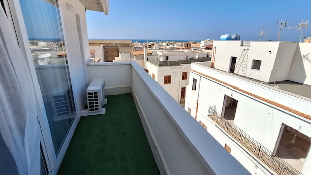 A balcony with a green artificial turf, white walls, and a view of the sea and other buildings. - Room-triple Double Room (Terrasini)