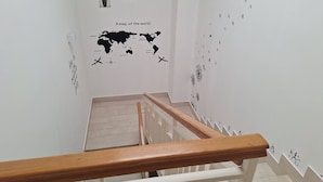 A staircase with a wooden handrail leading to a landing with a world map and potted plants. - Room-triple Double Room (Terrasini)