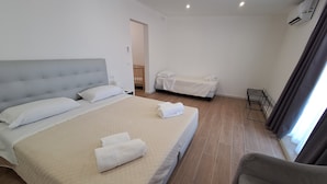 A hotel room with a large bed, a smaller bed, a chair, and a metal rack. - Room-triple Double Room (Terrasini)