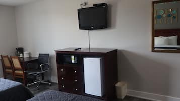 Una habitación de hotel con una cama, un escritorio con computadora, un refrigerador, un cesto de basura y un televisor montado en la pared.