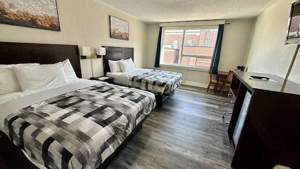 Quarto de hotel com duas camas, uma escrivaninha e uma janela com vista para edifícios.