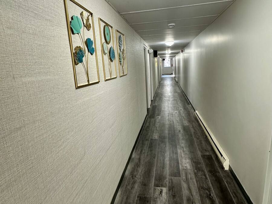Un pasillo largo y estrecho con suelo de madera y paredes grises claras. Se observan tres obras de arte enmarcadas en la pared izquierda.