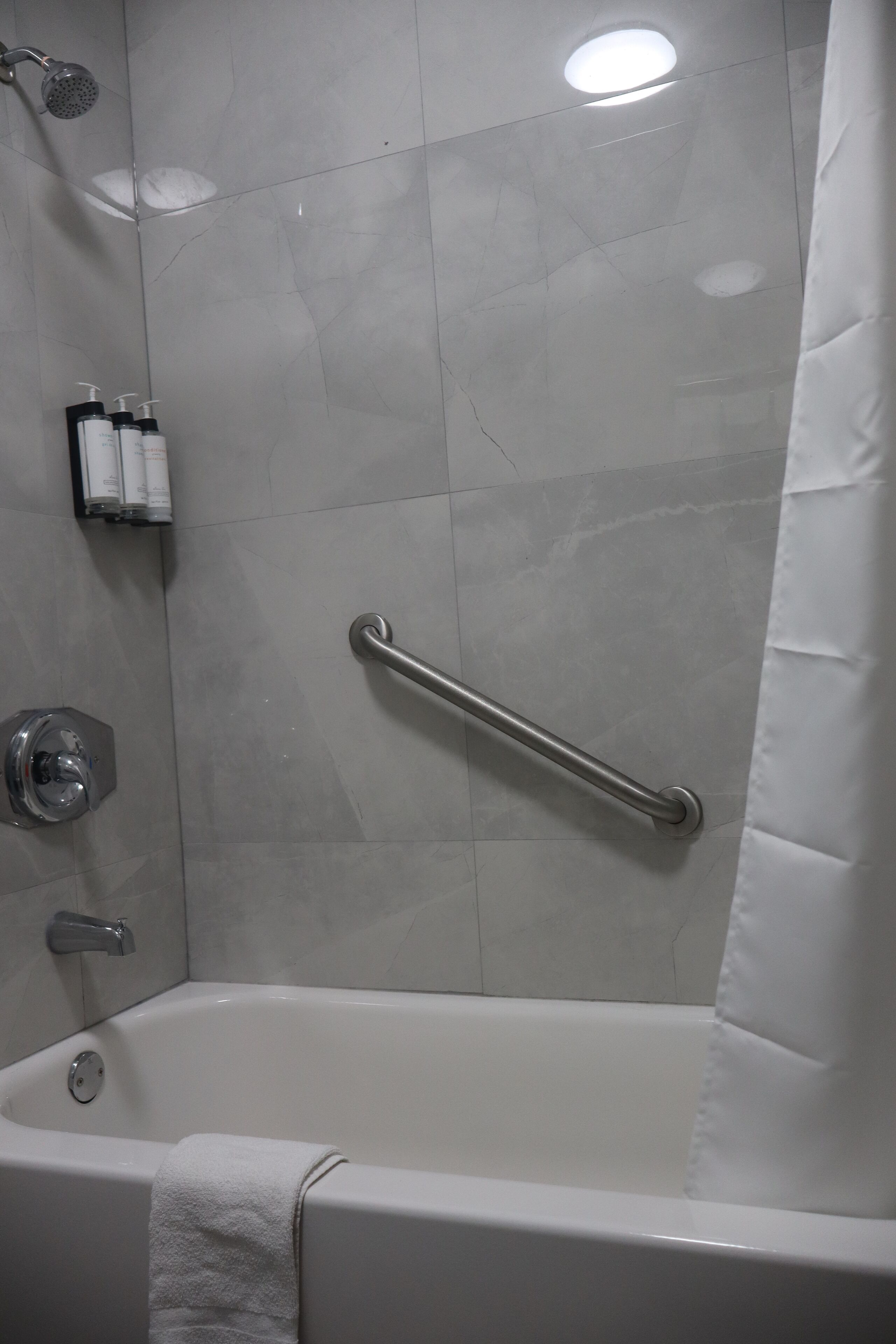 A modern bathroom with a bathtub, a showerhead, a grab bar, and a towel rack.