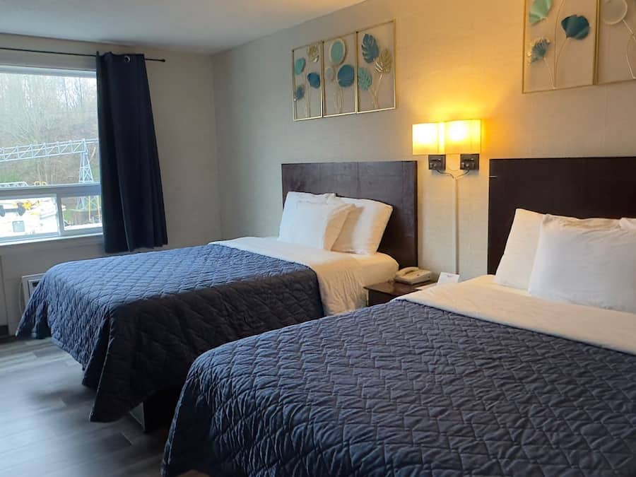 Habitación de hotel con dos camas, una ventana con vista a una obra en construcción y una obra de arte en la pared.