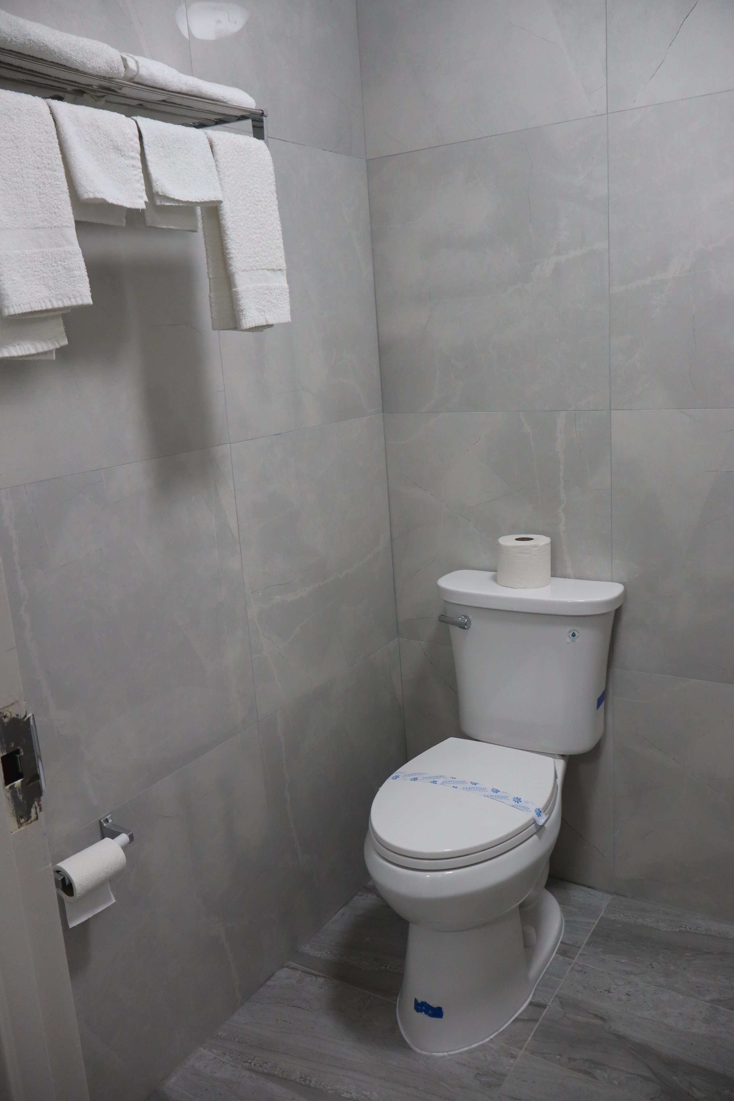 Un baño con inodoro, toallero con toallas y dispensador de papel higiénico.