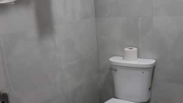 Un baño con inodoro, toallero con toallas y dispensador de papel higiénico.