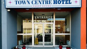Entrada do Town Centre Hotel com quatro bandeiras do Canadá, uma placa de sinalização e plantas em vasos.