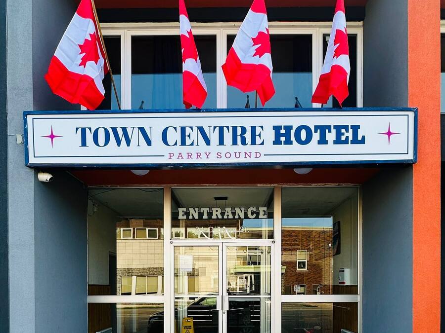 The Town Centre Hotel entrance with four Canadian flags, a signboard, and potted plants at the entrance.