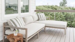 En vit terrass med trägolv, en vit soffa med kuddar och en trädstam som används som bord, med ett glas på.