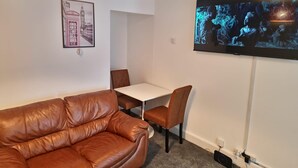 Una sala de estar con un sofá de cuero marrón, una mesa blanca y un televisor montado en la pared.