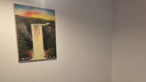 Una habitación de hotel con una cama, un cuadro de una cascada y una almohada blanca.