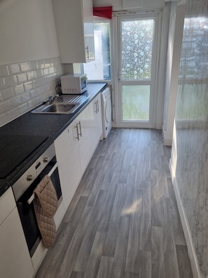 A modern kitchen with a sink, microwave, oven, and a window with a view of greenery.