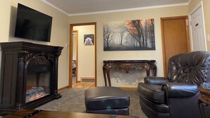 Una sala de estar con chimenea, televisor, un cuadro y un sillón de cuero.