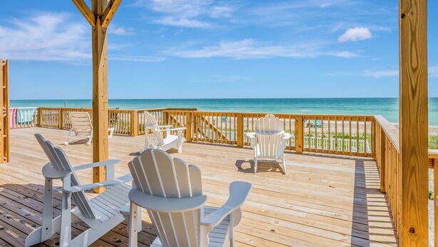 Terraza de madera con sillas Adirondack mirando hacia la playa.