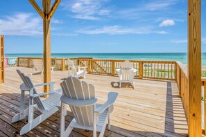 A wooden deck with Adirondack chairs facing a beach.