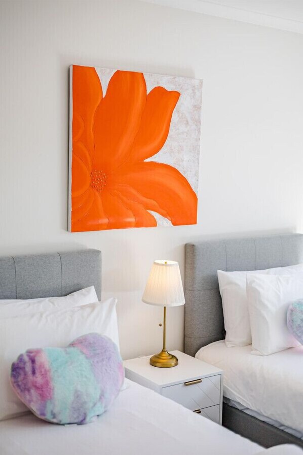 A hotel room with two beds, a nightstand with a lamp, and a large orange flower painting on the wall.