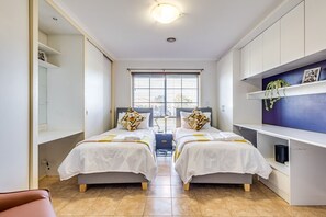 Une chambre moderne avec deux lits, un bureau et une fenêtre équipée de stores.