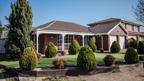 A two-story house with a covered front porch, a garage, and a well-maintained lawn with various shrubs and a tall tree. - StayAU Tranquil 4BR Lakeside Retreat in Seabrook (Seabrook)