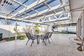 Une terrasse extérieure dotée d’un espace abrité, d’une table avec des chaises et d’un balai posé sur le sol.
