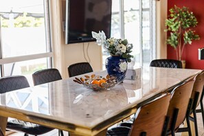 A dining area with a marble table, black cushioned chairs, a decorative bowl with flowers, and a television mounted on the wall.