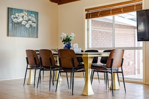 A dining area with a table and chairs, a painting on the wall, and a window with blinds.