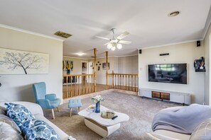 Ein geräumiges Wohnzimmer mit großem Fernseher, Deckenventilator und einer Treppe, die zu einer oberen Ebene führt.