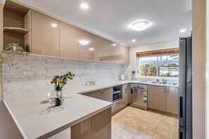 Een moderne keuken met een marmeren aanrechtblad, roestvrijstalen apparatuur en een raam met uitzicht op groen.