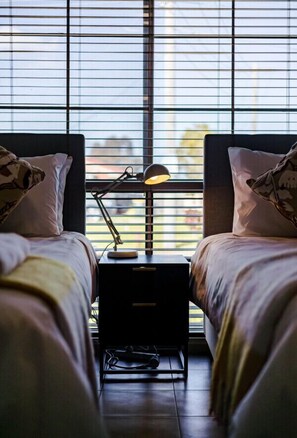 Ein Schlafzimmer mit zwei Betten, einem Nachttisch mit Lampe und einem Fenster mit Jalousien.