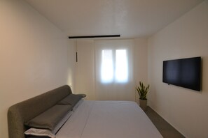 A bedroom with a bed, a TV mounted on the wall, and a window with curtains. - Nuovo Fiore (Pesaro)