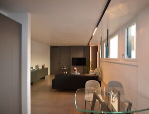 Ein modernes Wohnzimmer mit einem Glastisch, einer Couch und einem an der Wand befestigten Fernseher.
