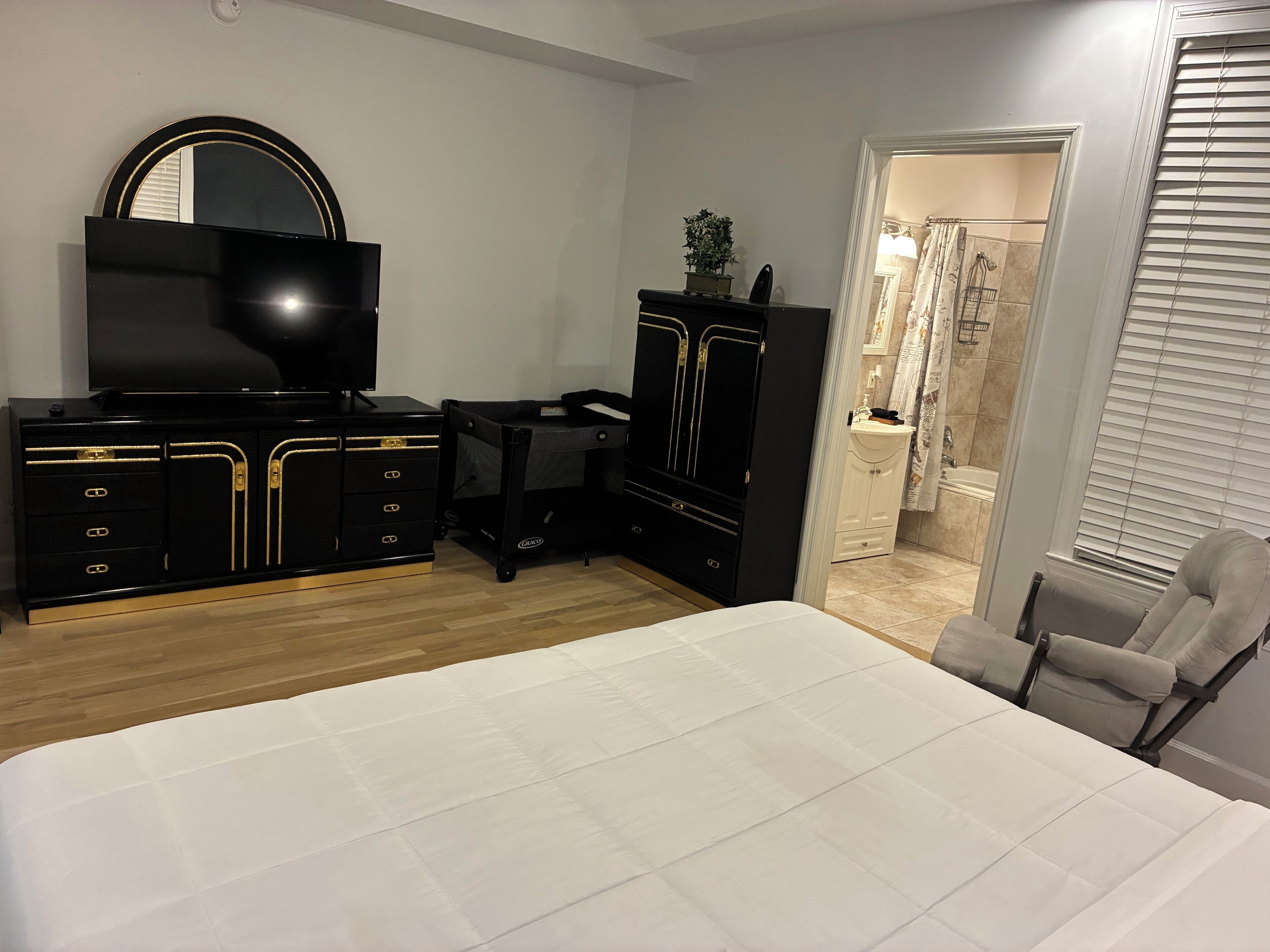 Een slaapkamer met een bed, een televisie, een kledingkast, een bureau en een badkamer zichtbaar door een open deur.