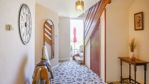 A hallway with patterned flooring, a wooden bench, a clock, a staircase, and a table with a vase. - The Lodge at Harvest Farm (Ludlow)