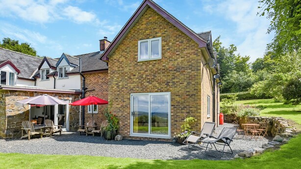 A two-story house with a brick exterior, a patio with outdoor furniture, and a large sliding glass door. - The Lodge at Harvest Farm (Ludlow)