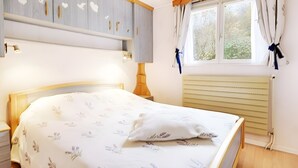 A bedroom with a bed, a nightstand, a window with curtains, and a radiator.